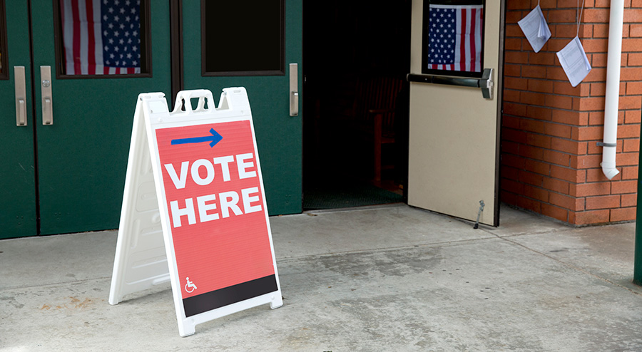 Image of a polling place with a "vote here" sign out front