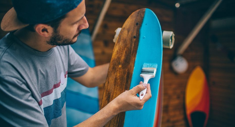 Photo of a man painting a skateboard.