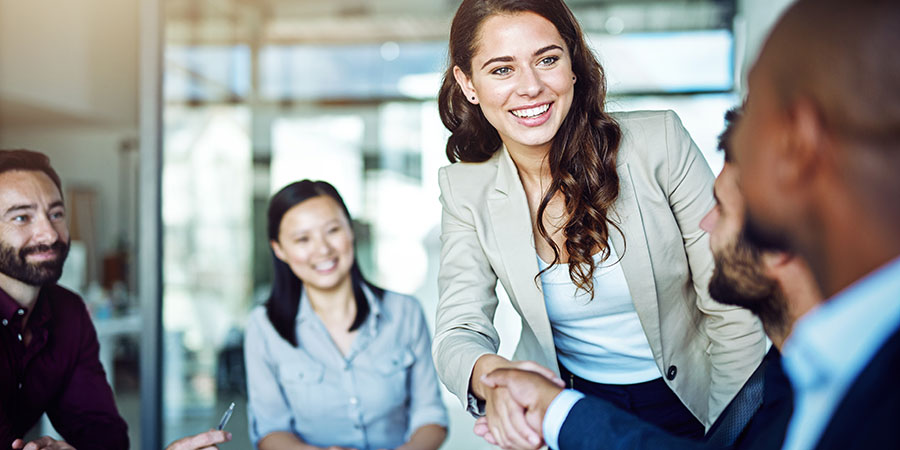 Young woman in an office meeting room with co-workers, shaking hands with one of them.