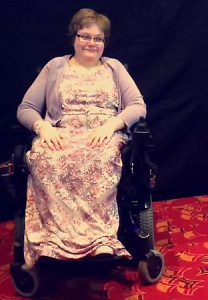 Stacy, wearing a floral dress, sitting in a wheelchair.